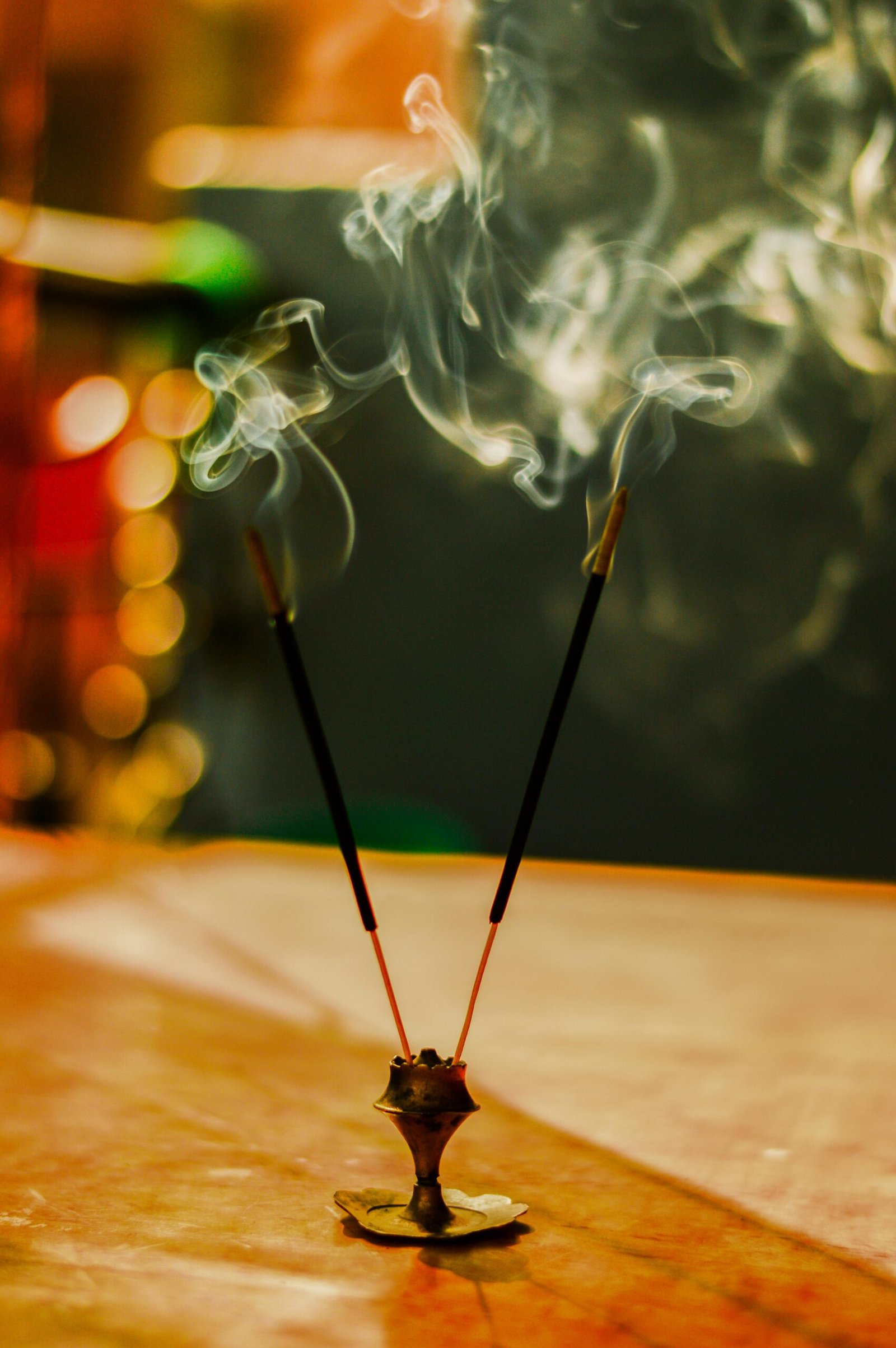 Artistic close-up of lit incense sticks with smoke swirling in a warm, blurred background.