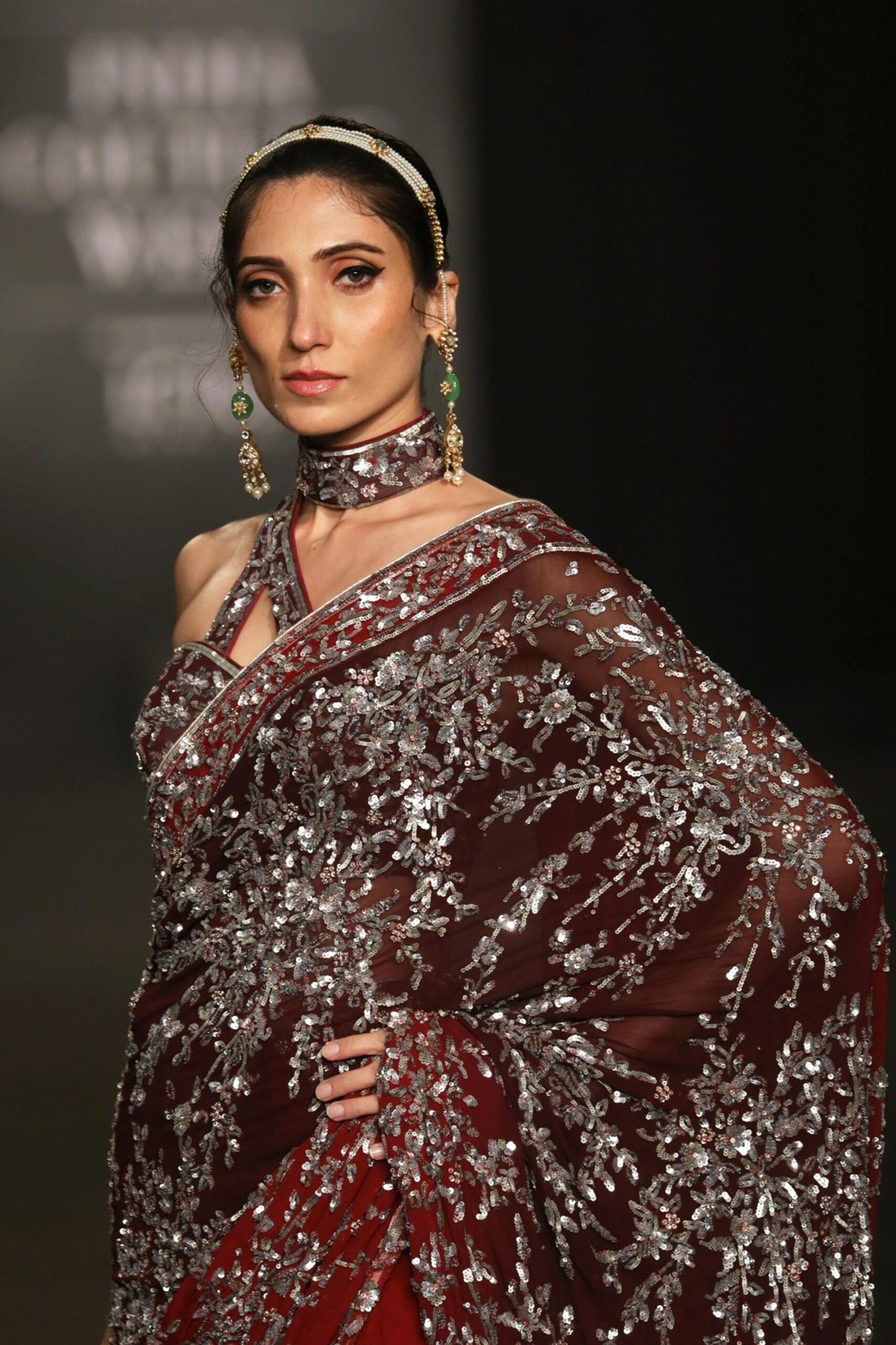 A woman elegantly poses in a red and silver sari with intricate embroidery during a fashion show in New Delhi.