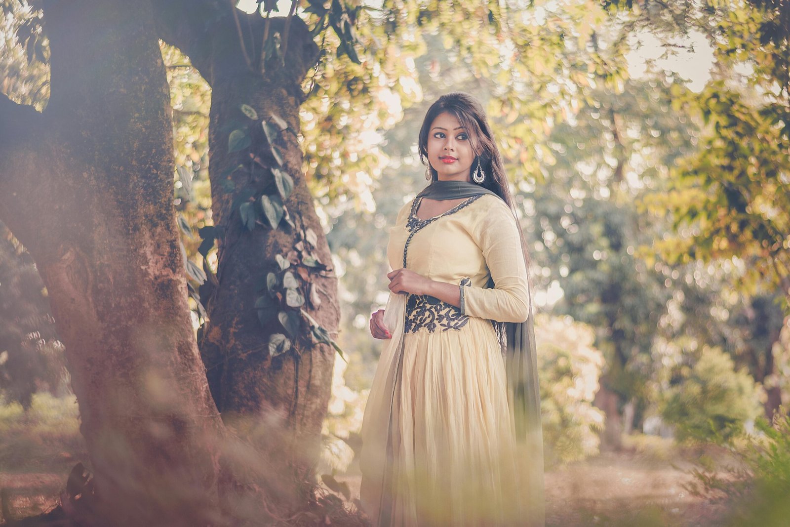 Portrait of a woman in traditional South Asian attire standing outdoors under trees.